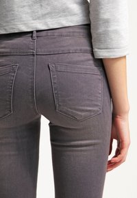 Vaqueros de denim gris con un ajuste ceñido, que cuentan con dos bolsillos traseros y una textura suave, estrechándose en los tobillos, adornados con costuras mínimas.