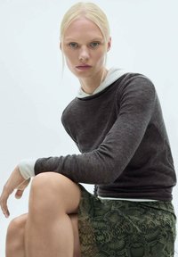 Donkergrijze lange mouw top, gelaagd over een witte blouse met kraag, gecombineerd met een groene slangenhuidprint rok, zittend gepresenteerd. Vloeiende texturen zijn duidelijk zichtbaar.