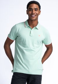 Jasnozielona koszulka polo z klasycznym kołnierzykiem, krótkimi rękawami i kontrastującymi czerwonymi akcentami na kołnierzyku i mankietach rękawów.