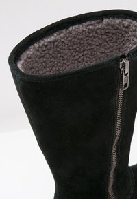 Botte d'hiver en suède noir avec fermeture éclair latérale et doublure en polaire douce grise à l'intérieur de la tige.