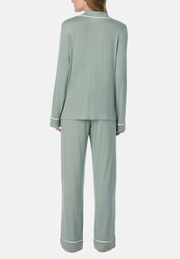 Lichtgroene pyjama set gemaakt van zachte stof, met lange mouwen en een broek met witte accent piping langs de randen.