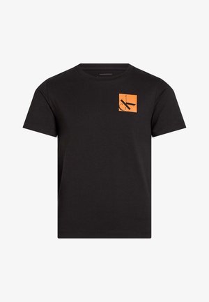 Camiseta negra de algodón con cuello redondo y mangas cortas. Presenta un logo cuadrado naranja con un "CK" estilizado en negro. Textura suave.