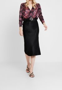 Mehrfarbiges Schlangenhaut-Bluse mit V-Ausschnitt, kombiniert mit einem glatten schwarzen Satin-Midirock und schwarzen Riemchenhemdchen.