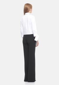 Camicia bianca tagliata con maniche lunghe arrotolate e pantaloni neri a gamba larga. Tessuto liscio con una vestibilità sartoriale, vista posteriore.