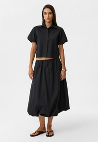 Zwarte cropped top met korte pofmouwen, gecombineerd met een bijpassende zwarte rok met hoge taille. Beide gemaakt van lichtgewicht stof met een soepele textuur.