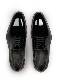 Paar schwarze glänzende Lackleder-Abendschuhe mit Schnürsenkeln, von oben auf weißem Hintergrund betrachtet.