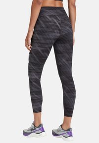 Leggings neri a vita alta con un motivo geometrico, realizzati in un tessuto elasticizzato, abbinati a scarpe da ginnastica grigie e viola.