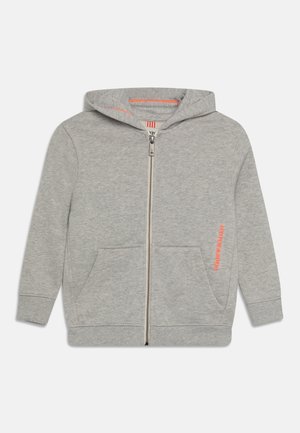 Sweat à capuche gris clair zippé avec poches avant, manches longues et texte orange « Scotch & Soda » en bas à droite.