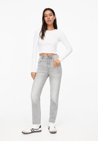 Lysegrå højtaljede jeans med lige ben, kombineret med en hvid langærmet cropped top og hvide sneakers med sorte detaljer.