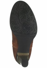 Bottines en daim marron avec une semelle en caoutchouc à motifs floraux. Le talon est bas, avec une finition lisse et un accent texturé.