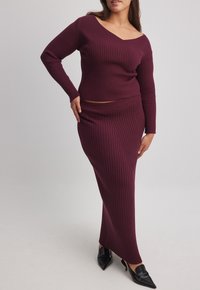 Burgundy ribbad stickad topp med avskuren halsringning och långa ärmar, matchad med en lång kjol och svarta spetsiga klackar.