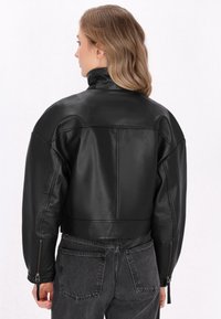 Zwarte leren cropped jack met hoge kraag, verlaagde schouders en ritssluitingen bij de mouwen. Soepele textuur en minimalistisch ontwerp.