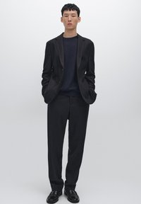 Černý přizpůsobený blazer přes námořnický svetr, doplněný o odpovídající kalhoty a černé boty. Hladká látka, slim fit a minimalistický design.