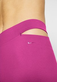 Lila högmidjade leggings med utskärning och liten logotyp. Slät textur med en jämn yta.