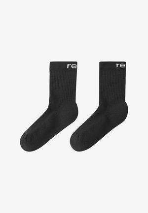 Para czarnych skarpetek za kostkę z białym fragmentem tekstu "re" blisko górnej krawędzi na jednolitym białym tle.