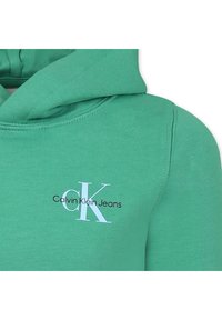 Felpa verde realizzata in tessuto di cotone misto con tasca a marsupio frontale. Presenta un logo bianco: "Calvin Klein Jeans" e "CK" in colori a contrasto.