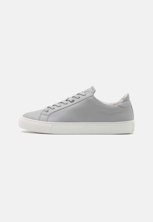 Lage grijze sneaker met witte rubberen zool en veters, getoond vanaf de zijkant op een effen lichte achtergrond.
