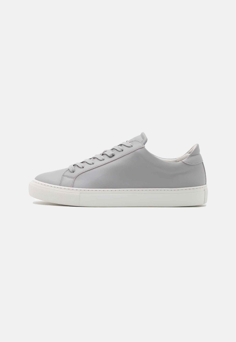 Baskets basses grises avec semelle blanche en caoutchouc et lacets, vues de profil sur un fond clair uni.