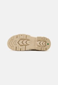 Semelle de chaussure en caoutchouc beige avec un motif de semelle présentant des formes en zigzag et circulaires. Comprend un accent vert près du talon.