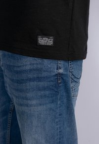 Musta T-paita, jossa on teksturoitu pinta ja helman lähellä "Petrol Ind" -tarran. Yhdistetty vaaleansiniset farkut, joissa on hienovaraisia haalistumia.