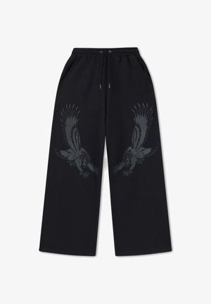 Černé kalhoty s širokými nohavicemi, stahovací šňůrkou v pase a tmavými motivy orla potisknutými na přední horní části nohavic.