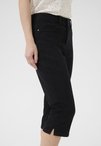 Pantaloni neri cropped con una vestibilità slim, realizzati in morbido cotone. Presentano una gamba leggermente svasata e piccole fessure laterali all'orlo.