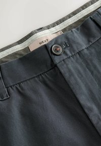 Grå stofbukser med en glat tekstur, der har en brun knaplukning og et label fra "NEXT" indeni livet.