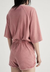 Rosa fleece lounge set bestående av en kortärmad topp med avslappnad passform och shorts med elastiskt midjeband, allt i ett mjukt, strukturerat material.