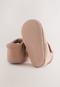 Chaussures pour bébé en daim rose doux avec semelles cousues et une bride Velcro, présentées vues de dos et de la semelle sur un fond neutre.