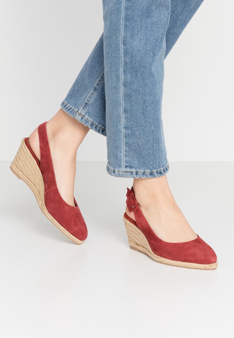 Sandales compensées en suede rouge avec un design à talon slingback, présentant un talon en jute tissé et une boucle décorative sur la sangle.
