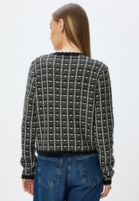Pull en tricot à motif noir et blanc avec un col rond et des poignets et un ourlet côtelés, présentant une coupe boxy et une finition texturée.
