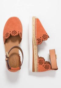 Sandali espadrille in suede arancione con design floreale intagliato, una cinghia alla caviglia in pelle marrone e dettagli in corda intrecciata su una suola bianca.
