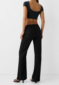 Black wide-leg pants made of lightweight fabric, paired with a cropped dark gray top featuring a low back. Open-toe black sandals.
