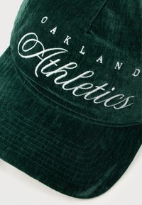Zelená kordurová bejzbolka s vystúpeným bielym vyšitým textom "Oakland Athletics." Mäkkučký materiál s pevným tvarom.