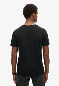 Czarna koszulka z krótkim rękawem i okrągłym dekoltem, wykonana z miękkiego materiału, o gładkiej fakturze i luźnym kroju z tyłu, z minimalnymi przeszyciami.