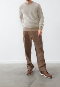 Maglione a maglia testurizzata beige, pantaloni plettati marroni e scarpe stringate marroni con suole bianche. Design semplice, vestibilità casual, accenti minimal.