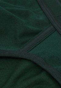 Głęboka zielona tkanina o gładkiej teksturze, z kontrastującymi ciemnymi szwami i brzegami, przedstawiona w złożonym układzie.