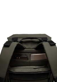 Intérieur d'un sac à dos vert olive avec plusieurs compartiments, y compris une poche en maille et des sections rembourrées pour un téléphone et un carnet. Tissu texturé.