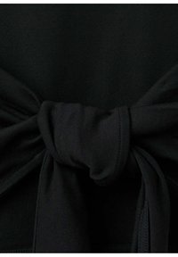 Gros plan d’un tissu noir noué, montrant la texture et les plis du matériau sur un fond sombre.