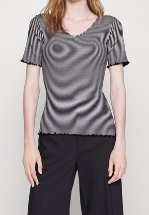 Femme portant un haut ajusté à manches courtes rayé noir et blanc avec bords volantés, associé à un pantalon noir ample.