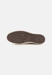Semelle de chaussure en caoutchouc marron avec un motif de bande de roulement présentant des formes géométriques. Les bords sont de couleur blanc cassé avec une finition lisse contrastante.