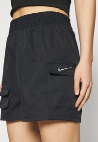 Svarta sportshorts med elastisk midjeband, utrustade med två sidofickor och en liten metallisk logotyp på ficklocket.