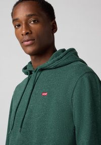 Groene Levi's hoodie van een gestructureerde stof, met een voorzak en een klein rood logo-opdruk op de linkerkant van de borst.