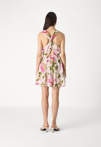 Blumenmusterkleid mit einem geknoteten Rückendesign, das pinke und grüne Farbtöne auf einem hellen Hintergrund zeigt. Ein gerüschter Saum sorgt für Textur.