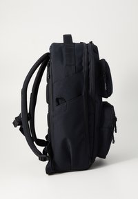 Sac à dos en nylon noir avec un dos rembourré et des bretelles réglables, comportant plusieurs poches zippées et un design élégant et structuré.
