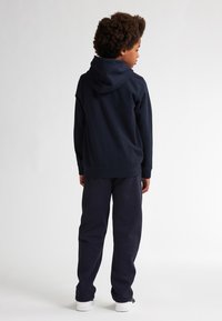 Marineblauwe hoodie met een kangoeroezak en een capuchon, gecombineerd met bijpassende marineblauwe joggingbroek en witte sneakers, gezien vanuit de achterkant.