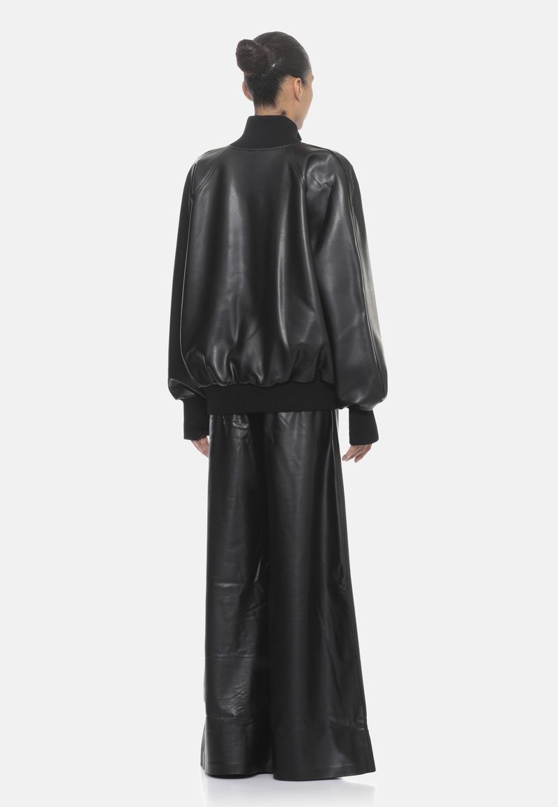 Giubbotto bomber in pelle nera con colletto e polsini a coste, abbinato a pantaloni in pelle nera a gamba larga. Texture liscia e vestibilità over.