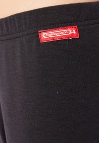 Leggings termici neri realizzati in tessuto morbido e elastico, con un vistoso etichetta rossa con "THERMOLACTYL 4" cucita sulla vita.