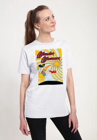 Witte t-shirt met een grafische print in felle gele, blauwe en rode kleuren, die een superheld in actie toont met een zonmotief.