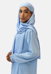Hijab et tunique bleu clair avec de longues manches fluides. Le tissu a une texture lisse avec un léger éclat et des accents argentés le long des bords.